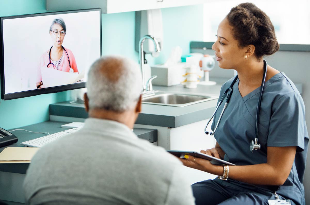 A nurse and a patient looking at a doctor on a computer screen