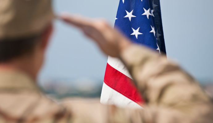 Close-up of US military personnel saluting American flag.
