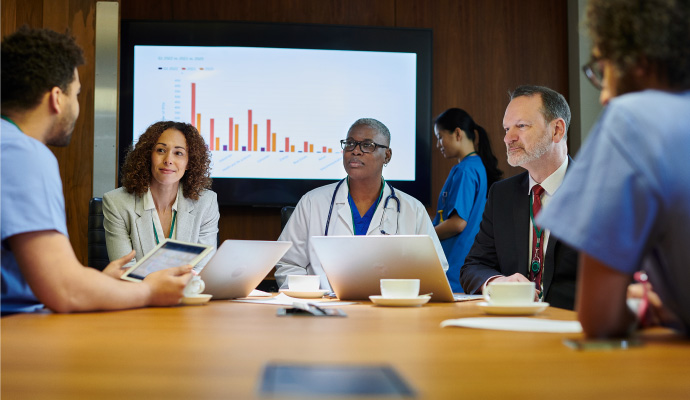 Medical professionals in a meeting with presentation in background.