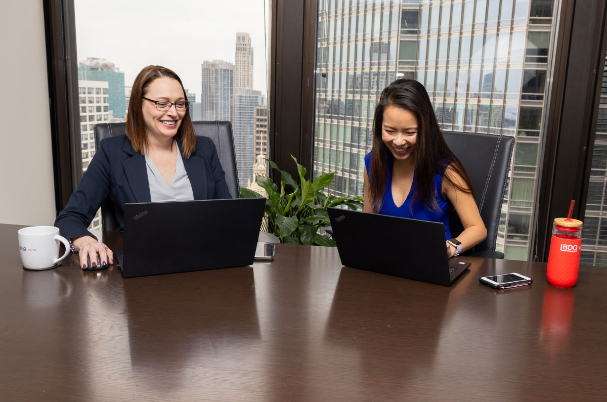 Two BDO professionals working on their laptops at a conference table
