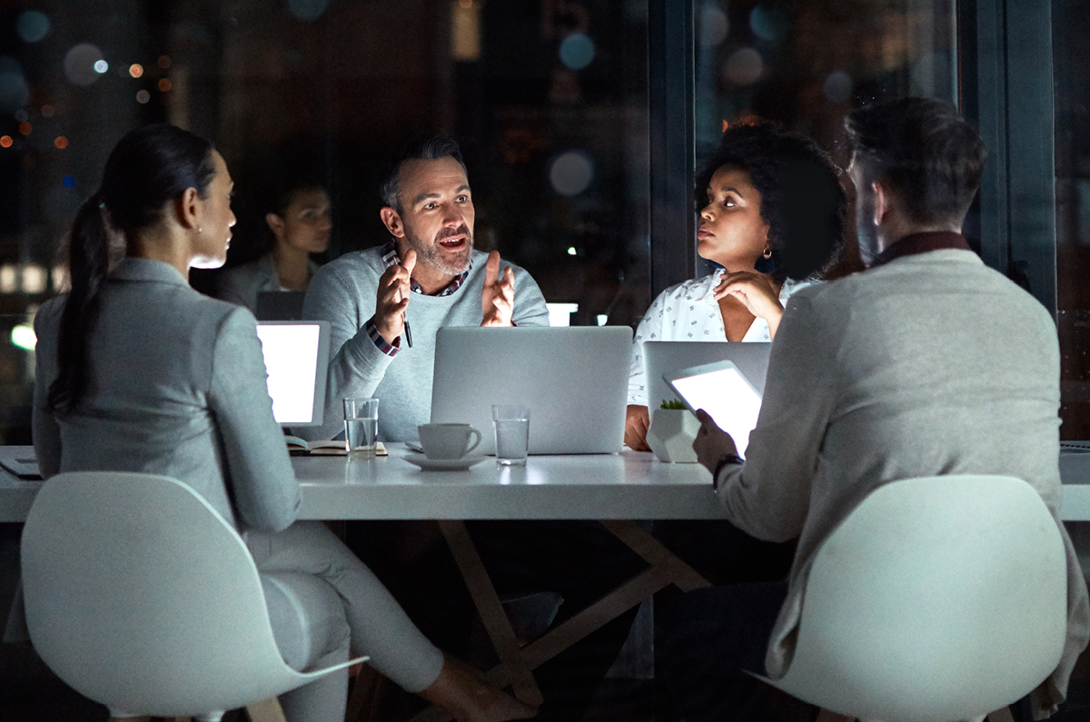 Image with four people sitting around a table with computers and talking